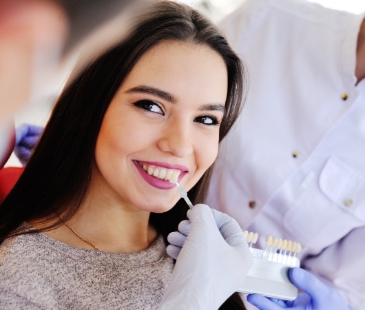 Derry cosmetic dentist holding row of veneers next to smile of young woman in dental chair