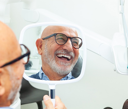A man smiling in the mirror at the dentist’s office