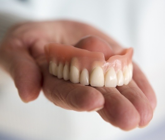 Person holding full upper denture in their hand